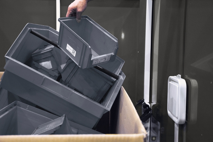 Das Kanban RFID Gate von innen voller grauer Plastikbehälter, von denen einer von einer Hand gerade hineingelegt wird.